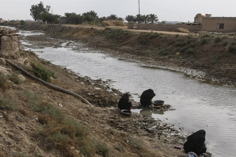 نسوة يملأن القدور من نهر العز بمحافظة ميسان جنوب العراق الذي شهد انخفاضا بجريانه بسبب قطع إيران للمياه العذبة خلال السنوات الماضية (الجزيرة نت)