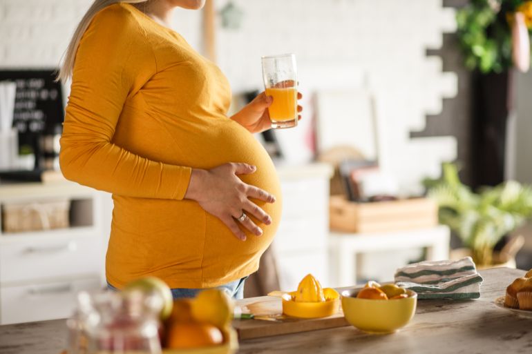 Midsection of future mother drinking a freshly-squeezed orange juice to keep her immune system healthy and strong during her pregnancy. بدائل للقهوة تستمتعين بها خلال الحمل