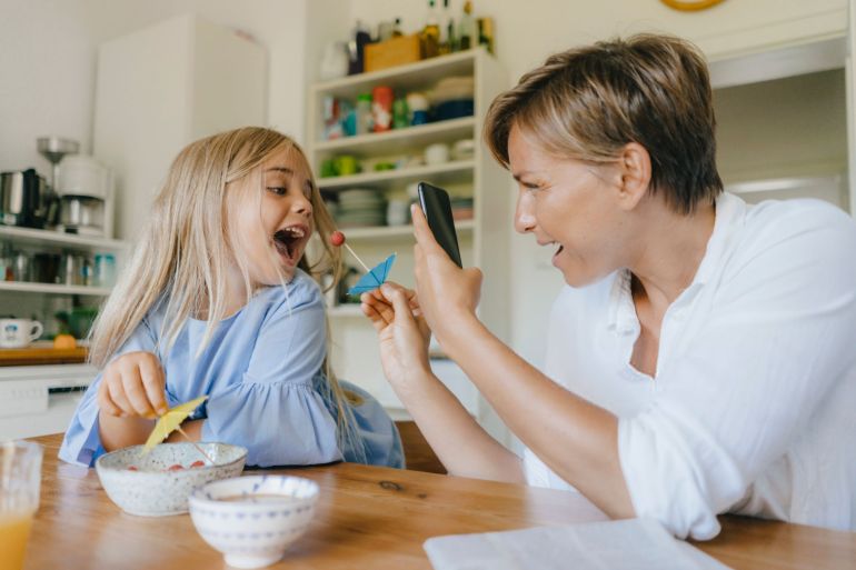 Happy mother and daughter having fun at table at home taking smartphone picture - stock photo