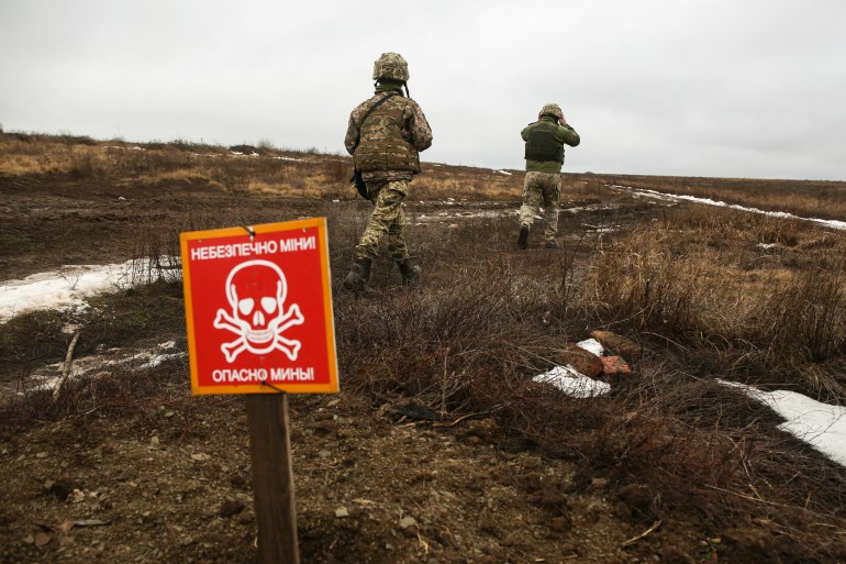 An Ukrainian Military Forces serviceman walk past a metal plate which reads as "Caution mines" on the frontline with Russia-backed separatists near Luganske village, in Donetsk region on January 11, 2022. - Ukraine said on January 11, 2022 it welcomes "efforts" by the West and Russia to ease tensions over Ukraine after a week of high-stakes diplomacy kicked-off in Geneva this week. (Photo by Anatolii STEPANOV / AFP)