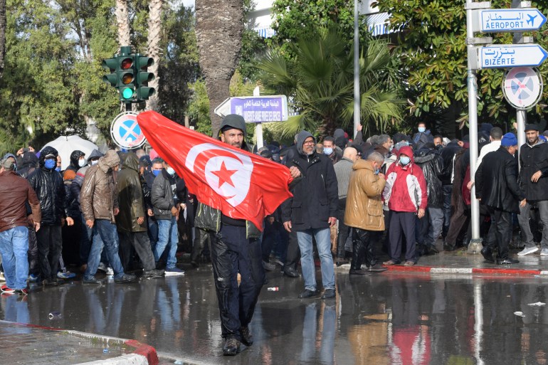 A Tunisian demonstrator waves his country's national flag during demonstrations against President Kais Saied, on the 11th anniversary of the Tunisian revolution in the capital Tunis on January 14, 2022. - Tunisian police used teargas today against hundreds of demonstrators who had defied a ban on gatherings to protest against President Kais Saied's July power grab. As the country marks 11 years since the fall of late dictator Zine El Abidine Ben Ali, hundreds of Saied's opponents staged rallies against his July 2021 power grab. (Photo by FETHI BELAID / AFP)
