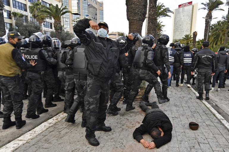A Tunisian policeman calls for a stretcher after a man collapsed during demonstrations against President Kais Saied, on the 11th anniversary of the Tunisian revolution in the capital Tunis on January 14, 2022. - Tunisian police used teargas today against hundreds of demonstrators who had defied a ban on gatherings to protest against President Kais Saied's July power grab. As the country marks 11 years since the fall of late dictator Zine El Abidine Ben Ali, hundreds of Saied's opponents staged rallies against his July 2021 power grab. (Photo by FETHI BELAID / AFP)