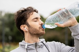 Close-up of young man drinking water and listening to music in park