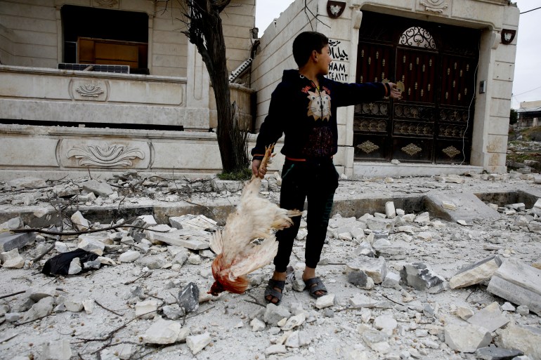 A Syrian boy removes a dead chicken from the debris of a building hit by an air strike in Idlib