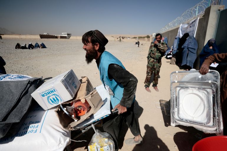 FILE PHOTO: An UNHCR worker pushes a wheelbarrow loaded with aid supplies for a displaced Afghan family outside a distribution center as a Taliban fighter secures the area on the outskirts of Kabul, Afghanistan October 28, 2021. REUTERS/Zohra Bensemra/File Photo