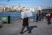 رجل يرتدي قناعا للوجه ويحمل صندوقًا بلاستيكيا خشية الإصابة بفيروس كورونا (الأوروبية)