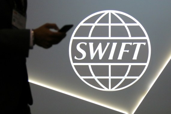 A man using a mobile phone passes the logo of global secure financial messaging services cooperative SWIFT at the SIBOS banking and financial conference in Toronto, Ontario, Canada October 19, 2017. REUTERS/Chris Helgren