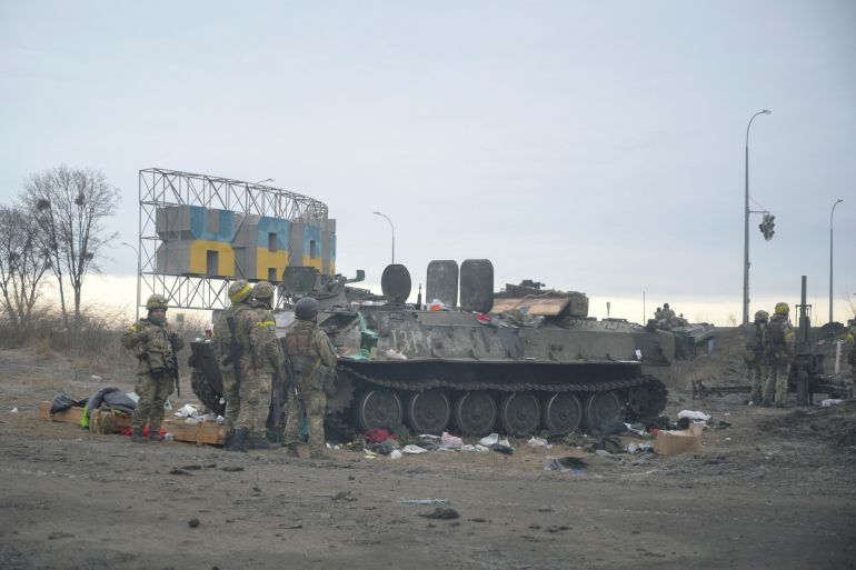 Ukrainian servicemen stand guard next to a destroyed armoured vehicle on the outskirts of Kharkiv
