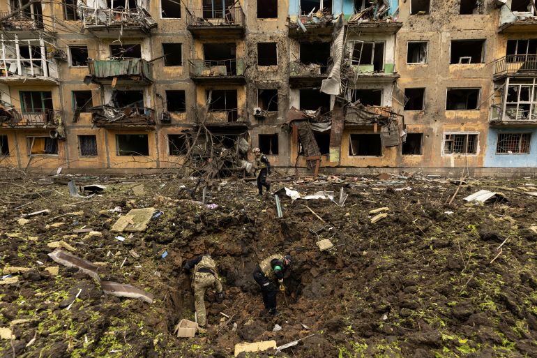 Ukrainian military personnel inspect the site of a missile strike in front of a damaged residential building in Dobropillia