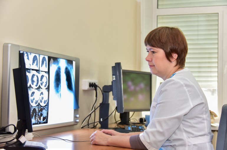 Experts in imaging and radiology study images of patients by computer monitors