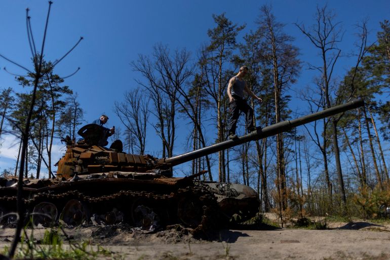 Local residents climb on top of a destroyed Russian tank, as Russia's attack on Ukraine continues, near Irpin