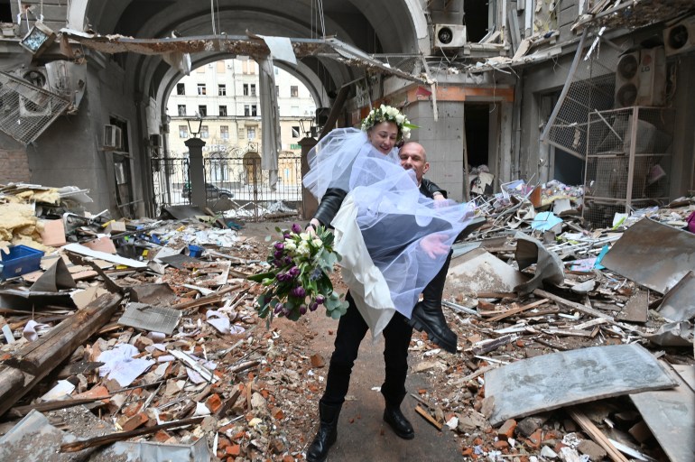 The newlyweds, medical volunteers, nurse in an oncology clinic and doctor before the start of the Russian invasion of Ukraine, Nastya Gracheva and Anton Sokolov, pose for a photograph in aruined courtyard of shopping and office complex in central Kharkiv on April 3, 2022. - From the beginning of the Russian aggression, they began to provide free medical care to those in need at home, and when they ran out of medicines, they began to collect money and purchase medicines for residents of the city who needed them. (Photo by Sergey BOBOK / AFP)