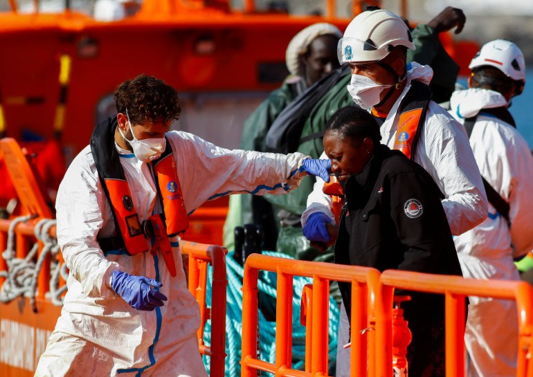 Rescuers help a migrant to disembark from a Spanish coast guard boat in the port of Arguineguin