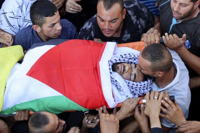 A mourner kisses the forehead of 17-year-old Kamel Alawnah during his procession in the West Bank village of Jaba, north of Jenin, on July 3, 2022. - A Palestinian teenager died after being shot by Israeli forces in the occupied West Bank a day earlier, Palestinian medical sources said. (Photo by JAAFAR ASHTIYEH / AFP)