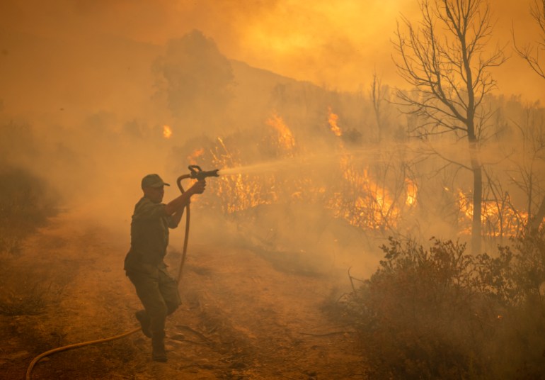 A Moroccan soldier sprays water from a hose on a forest fire near the Moroccan city of Ksar el-Kebir in the Larache region, on July 15, 2022. (Photo by FADEL SENNA / AFP)