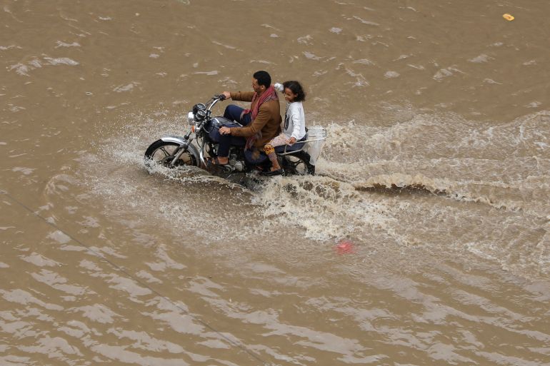 People ride a motorbike on flood water in the old quarter of Sanaa
