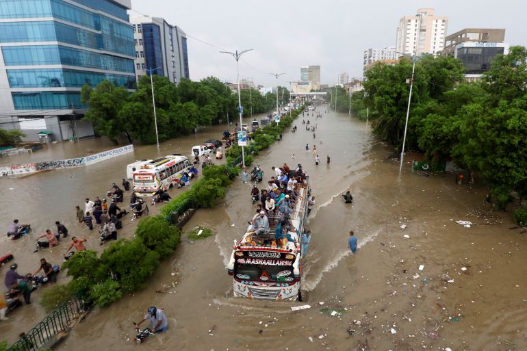 People sit atop a bus roof while others wade through the flooded road during monsoon rain, as the outbreak of the coronavirus disease (COVID-19) continues, in Karachi, Pakistan August 27, 2020. REUTERS/Akhtar Soomro TPX IMAGES OF THE DAY