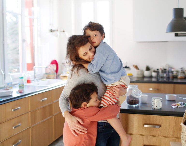 A mom hugging her sons in the kitchen GettyImages-651272126