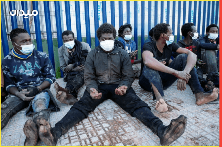 مهاجرون يجلسون خارج مركز مؤقت للمهاجرين بعد عبورهم السياج إلى مليلية (رويترز/أرشيف)