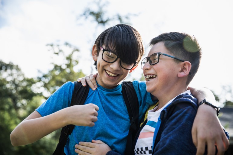 School age brothers laughing outdoors GettyImages-1058791954
