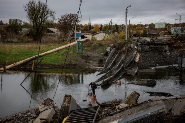 A man carries water bottles as he crosses a destroyed bridge in the frontline town of Bakhmut, in eastern Ukraine's Donetsk region, on October 27, 2022, amid Russia's invasion of Ukraine. - The eastern Ukraine town, known for its salt mines and vineyards, has been under attack for months by Russian forces, who are mostly on the defensive in other regions across Ukraine. (Photo by Dimitar DILKOFF / AFP)