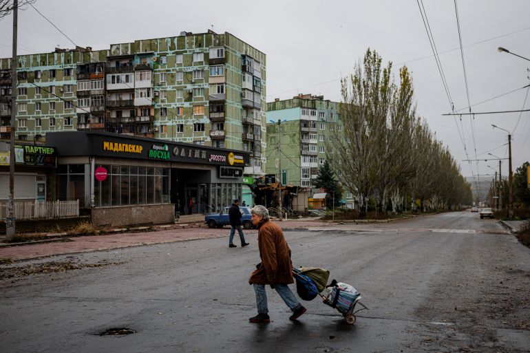 A woman pulls a cart while crossing a street in the frontline town of Bakhmut, in eastern Ukraine's Donetsk region, on October 27, 2022, amid Russia's invasion of Ukraine. - The eastern Ukraine town, known for its salt mines and vineyards, has been under attack for months by Russian forces, who are mostly on the defensive in other regions across Ukraine. (Photo by Dimitar DILKOFF / AFP)