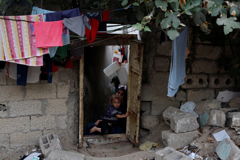 Khadija Kuhail holds her son, Mohanad Kuhail, one, in the doorway of their family home. 'If the dead could talk, they would tell us, get out of here,' said Kamilia who has lived in the cemetery for 13 years with her husband and a family now numbering six children. [Mohammed Salem/Reuters]
