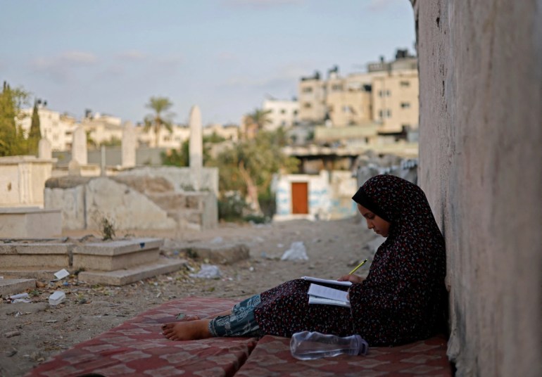 Lamis Kuhail, 12, studies for school in the Sheikh Shaban cemetery. 'I sometimes get invited by friends from school, but I can't invite them here, I am too shy to do that,' said Lamis. [Mohammed Salem/Reuters
