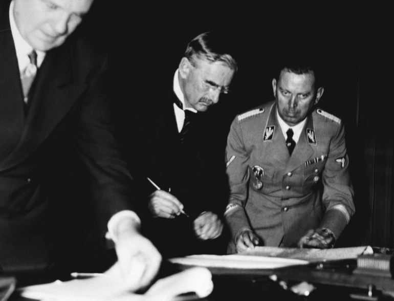 After long discussions the treaty for giving the Sudeten Districts from Czechoslovakia back to Germany was signed by the four statesmen Adolf Hitler, Benito Mussolini, Eduard Daladier and Sir Neville Chamberlain at the Fuehrerhouse at Munich on Sept. 30, 1938. Premier Neville Chamberlain rears the treaty over before signing. Left interpreter Dr. Paul Schmidt, Sir Neville Chamberlain and Hitler?s adjutant brigade leader Schaub. (AP Photo/Berlin Hoffman)