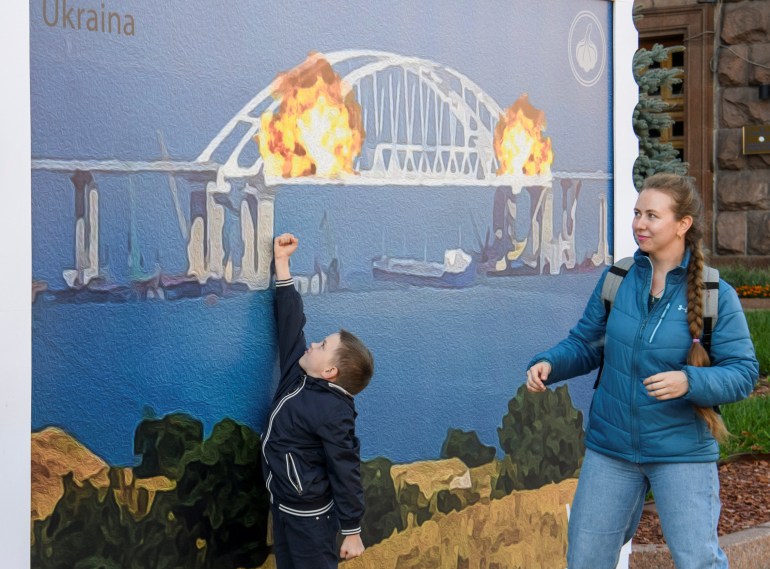 Boy reacts as he walks past an artwork depicting Kerch bridge on fire, in Kyiv