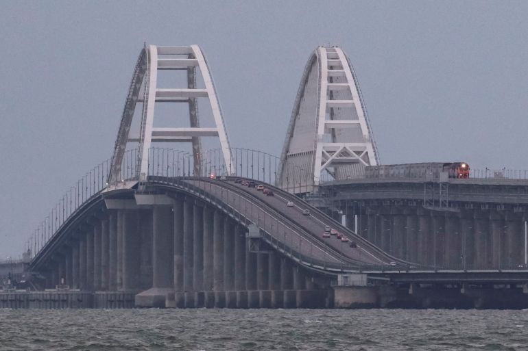 A passenger train and cars drive on the Kerch bridge, after an explosion destroyed part of it, in the Kerch Strait, Crimea