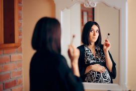 Pregnant Woman Applying Make-up in Front of a Mirror. Mother to be getting ready for a party