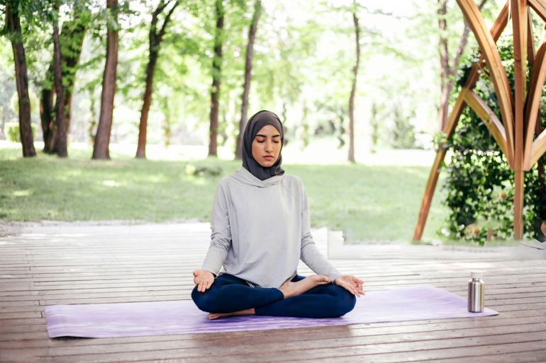 Young arab woman in hijab doing yoga on fitness mat outdoors in park at the summer. Peace, harmony and vitality concept. إمرأة تمارس رياضة التأمل Woman meditation exercises gettyimages-1407238121