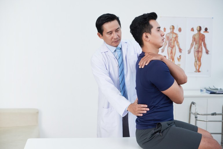 Mature osteopath palpating low back of patient in his office