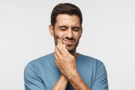 Tooth ache. Young man feeling pain, holding his cheek with both hands, suffering from bad toothache, having painful expression