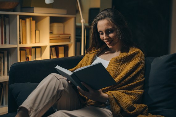 woman relaxing on sofa and reading book. evening moody ambience. she is enjoying time during weekend; Shutterstock ID 1941572155; purchase_order: ajnet; job: ; client: ; other: