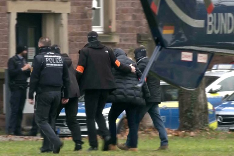 Police escorts a person in this screen grab from Reuters TV, after 25 suspected members and supporters of a far-right group were detained during raids across Germany, in Karlsruhe, Germany December 7, 2022. Reuters TV via REUTERS REFILE - CORRECTING ID