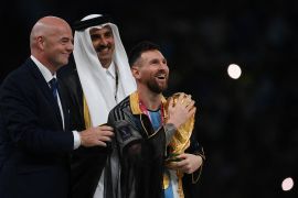 ميسي يحمل كأس العالم إلى جوار أمير قطر الشيخ تميم بن حمد آل ثاني ورئيس الفيفا جياني إنفانتينو (الجزيرة)