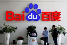 Men interact with a Baidu AI robot near the company logo at its headquarters in Beijing, China April 23, 2021. REUTERS/Florence Lo