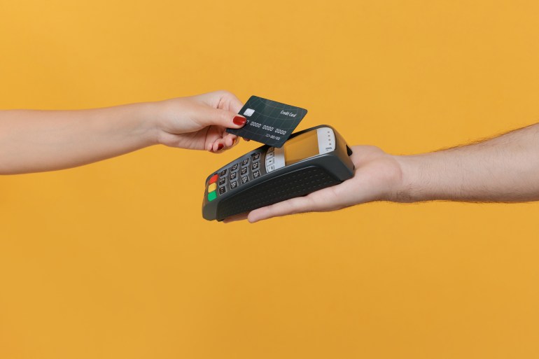 Close up cropped photo of female and male hold wireless modern bank payment terminal to process acquire credit card payments isolated on yellow background. Money, achievement, career wealth concept SS1728008851