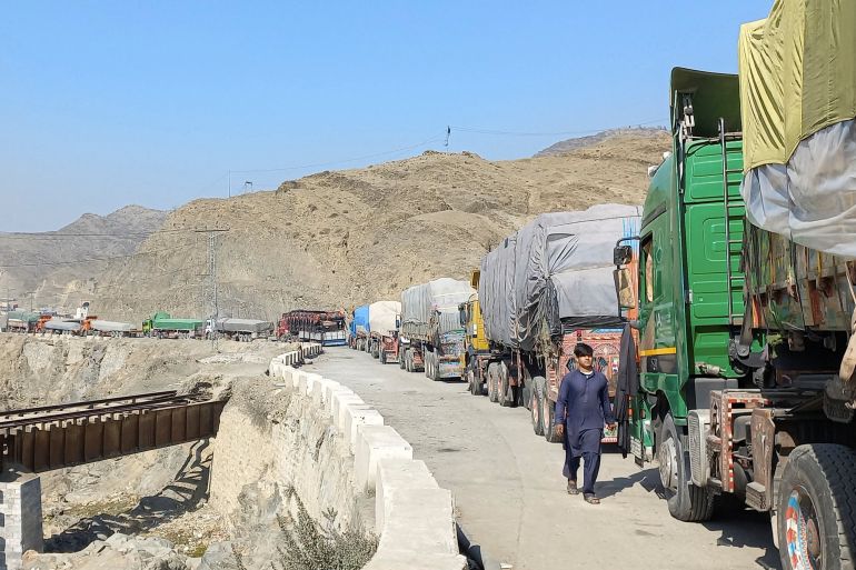 A man walks past trucks, loaded with supplies to leave for Afghanistan, seen stranded after Taliban authorities have closed the main border crossing in Torkham