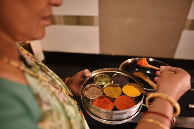 Women using Spices box with turmeric, chilli powder, Cardamom, mustard seeds, cumin seeds, curry masala for cooking