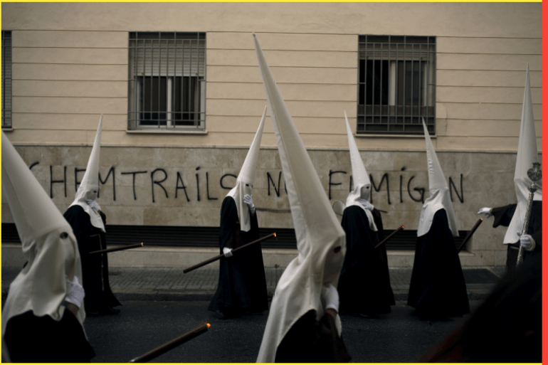 Penitents of "Dulce Nombre" brotherhood take part in a procession in the rain during Holy Week in Malaga, southern Spain, March 20, 2016. The graffiti on the wall reads, "Chemtrails. They fumigate us". REUTERS/Jon Nazca