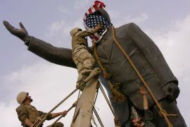 FILE - In this April 9, 2003, file photo, an Iraqi man, bottom right, watches Cpl. Edward Chin of the 3rd Battalion, 4th Marines Regiment, cover the face of a statue of Saddam Hussein with an American flag before toppling the statue in downtown Baghdad, Iraq. (AP Photo/Jerome Delay, File)
