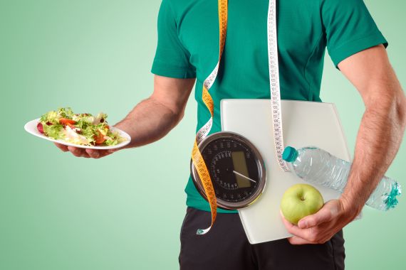 Man body dressed in sportswear with meter scale and water and salad plate on green isolated gradient background; Shutterstock ID 1881528892; purchase_order:ajnet; job:; client:; other: