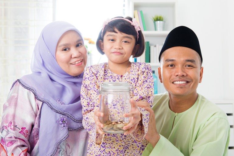 Southeast Asian Malay family saving money at home. Muslim father, mother and daughter living lifestyle. Islamic banking concept.