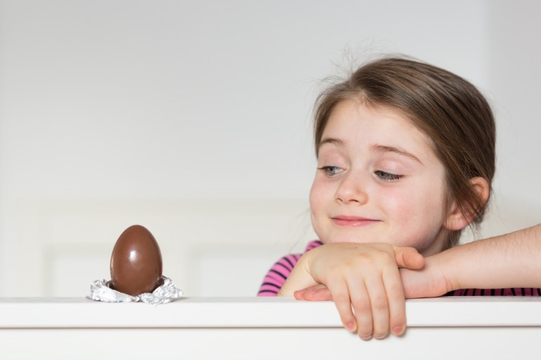 Kislány egy impish mosollyal nézi a csokoládé tojás