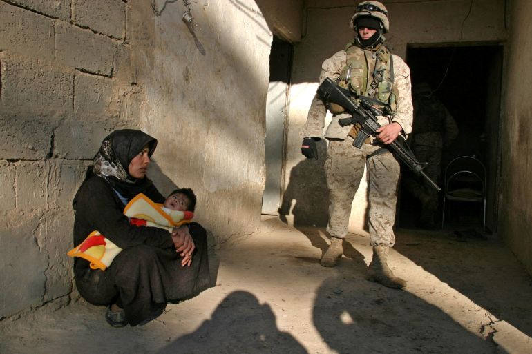 FILE PHOTO: A U.S. Marine watches a woman and her child during a series of raids to hunt arms and guerrilla suspects south of Baghdad, Iraq December 1, 2004. After a day of intensive sweeps by U.S. and British troops through farms and homes in a fertile stretch of the Euphrates Valley where support for Saddam Hussein was strong, a squad of Marines came under mortar fire close to the river. REUTERS/Thaier al-Sudani/File Photo