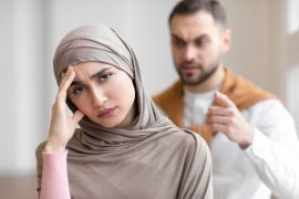 Angry Muslim Husband Shouting At Unhappy Wife While She Looking At Camera Standing At Home. Marriage And Relationship Crisis, Family Conflicts And Domestic Violence Concept. Selective Focus