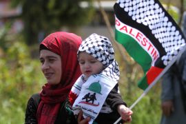 CORRECTS SECOND SENTENCE - A Palestinian woman who lives in Lebanon carries her child with the Palestinian flag during a protest marking the 67th anniversary of Nakba, or Catastrophe, in front of the United Nations peacekeepers (UNIFIL) headquarters in the costal town of Naqoura, southern Lebanon, Friday, May 15, 2015. Palestinians annually mark the Nakba Day, or the Day of the Catastrophe, when hundreds of thousands of Palestinians fled, or were expelled from their homes during the first Israeli-Arab war in 1948. (AP Photo/Mohammed Zaatari)